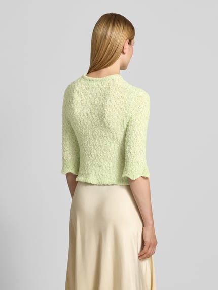 Frauenmodel trägt Strickjacke aus Lanawolle-Mix mit 3/4-Arm von Christian Berg Woman in Hellgrün, feine Struktur, Ganzkörperansicht Rückansicht, Slim-Fit, Rundhalsausschnitt, Knopfleiste, Stretch-Anteil, Rückenlänge bei Größe S 47 cm, Ärmellänge 42 cm.