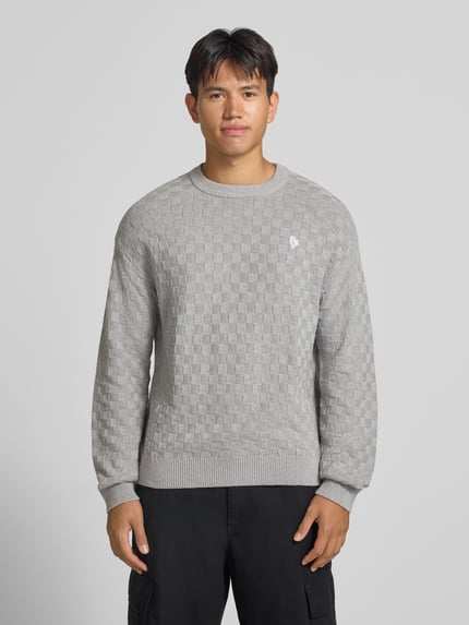 Männermodel trägt Regular Fit Strickpullover aus reiner Baumwolle mit Label-Detail von REVIEW, dezentes Karo-Muster, Ganzkörperansicht von vorne. Rückenlänge 67 cm, Ärmellänge 53 cm, elastische Abschlüsse.