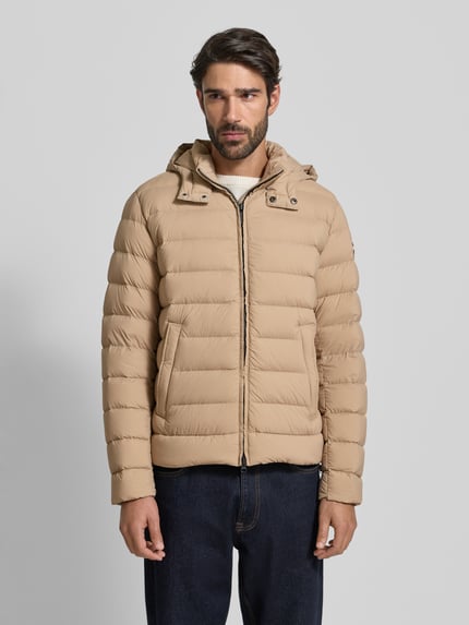 Männermodel trägt Steppjacke mit Kapuze von Colmar Originals in Beige, gesteppt, mit Reißverschluss und Taschen, Ganzkörperansicht von vorne. Regular Fit, Rückenlänge 66 cm, Schulterbreite 42 cm, Brustweite 56 cm, Ärmellänge 66 cm.