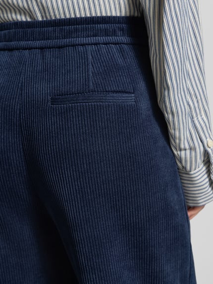 Frauenmodel trägt Relaxed Fit Cordhose mit Stretch-Anteil Modell 'KATE' von ICHI in Dunkelblau, feine Rippenstruktur, Nahaufnahme Hüfte, Elastischer Material-Mix, aufgesetzte Eingrifftaschen, Knopfverschluss, Bundweite S 38 cm, Innenbeinlänge S 72 cm.