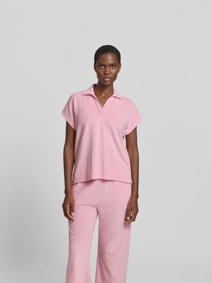 Vrouwenmodel draagt Poloshirt in Frottee-Optik van Juvia in roze katoenmix, relaxed fit, polokraag, korte mouw, badstoflook, Ganzkörperansicht von vorne
