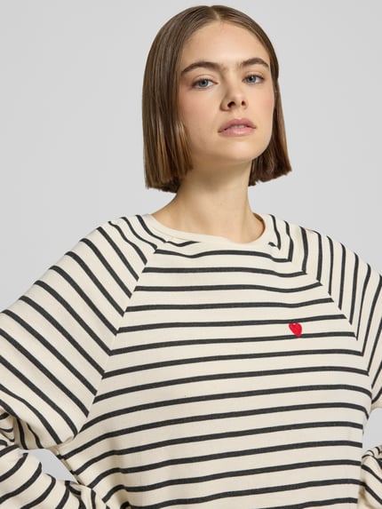 Kobiece modelka nosi Oversized Sweatshirt aus Baumwoll-Mix Modell 'GRETA' od Pieces, biało-czarne paski, czerwony detal, bawełniany miks, widok z przodu, zbliżenie na górną część ciała.