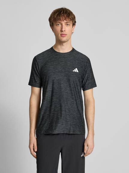 Männermodel trägt T-Shirt mit Label-Print von adidas Training in Schwarz mit dezentem Muster, Regular Fit, Nahaufnahme Oberkörper.