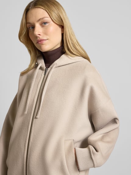 Frauenmodel trägt Oversized Sweatjacke mit Kapuze Modell 'DUNSTONE' von Drykorn aus Woll-Mix, Beige, Nahaufnahme Oberkörper.