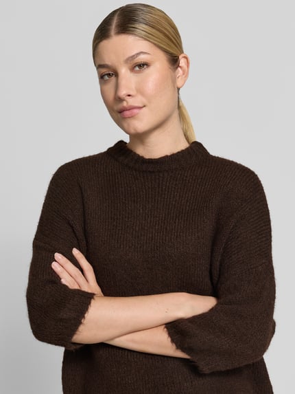 Vrouwenmodel draagt Relaxed Fit gebreide pullover met 3/4-mouw model 'BYOTIA' van b.young, materiaalmix met wol, ruglengte maat S 53 cm, mouwlengte 24 cm, donkerbruin, grof gebreide textuur, Nahaufnahme Oberkörper.