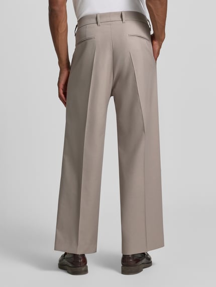 Männermodel trägt Wide Fit Hose mit Bügelfalten von Drykorn aus Baumwoll-Mix mit Stretch-Anteil, Beige, Ganzkörperansicht Rückansicht.