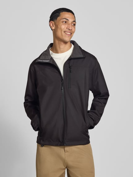 Männermodel trägt Regular Fit Jacke mit Stehkragen Modell 'Crew' von Helly Hansen in Schwarz, Logo-Print, Reißverschlusstaschen, Ganzkörperansicht von vorne. Herren Jacke, Stehkragen, Napoleontasche, Rückenlänge 73 cm, Schulterbreite 48 cm, Brustweite 56 cm, Ärmellänge 68 cm.
