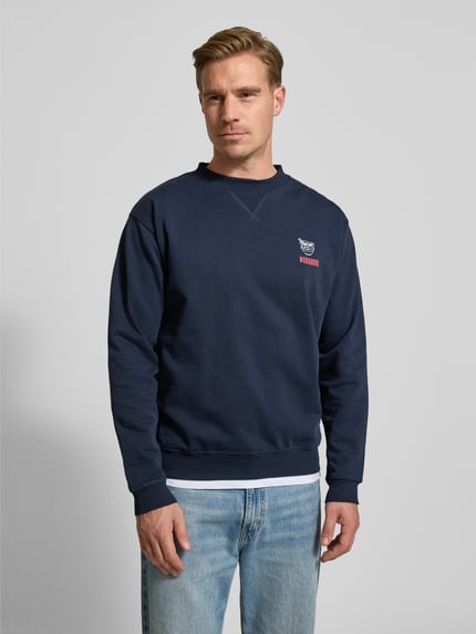 Männermodel trägt Sweatshirt mit Label-Print Modell 'Cane' von WOODBIRD in Dunkelblau, Baumwolle, Regular Fit, Nahaufnahme Oberkörper.