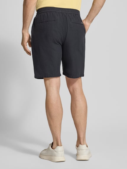Männermodel trägt Shorts aus Baumwoll-Leinen-Mix Modell 'FAVE' von Scotch & Soda, Regular Fit, elastischer Bund, Rückansicht, Kontext Herren Shorts, Bundweite 42 cm, Innenbeinlänge 21 cm, dunkle Farbe, glatte Textur. Ganzkörperansicht Rückansicht.