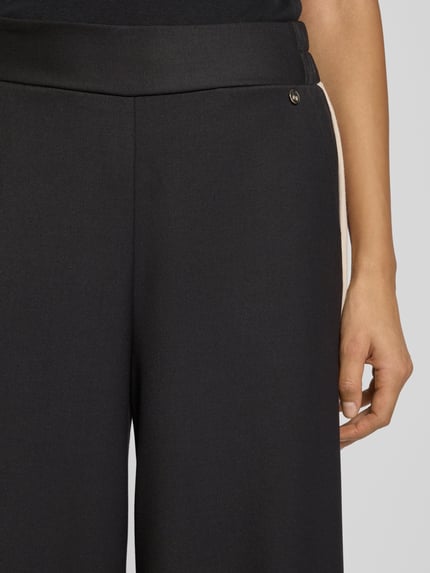 Kobiece modelka nosi Stoffhose mit weitem Bein und elastischem Bund od Rinascimento, czarne szerokie nogawki, elastyczny pas, tkanina z wiskozą, kieszenie boczne, detal z logo, zbliżenie na górną część spodni.