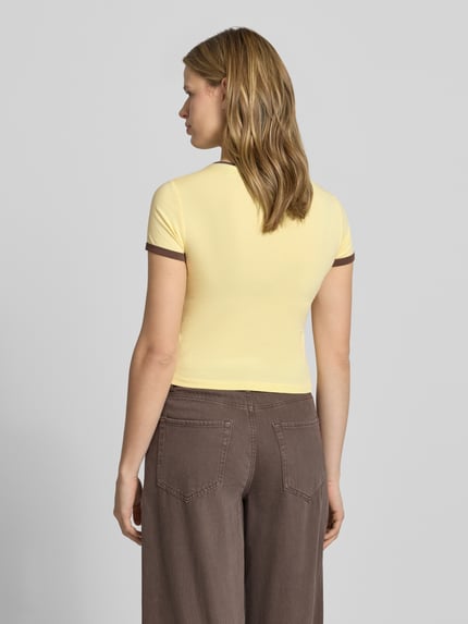 Frauenmodel trägt Slim Fit T-Shirt mit Statement-Print Modell 'Molly' von Noisy May in Gelb-Braun, elastischer Baumwoll-Mix, Ganzkörperansicht Rückansicht.