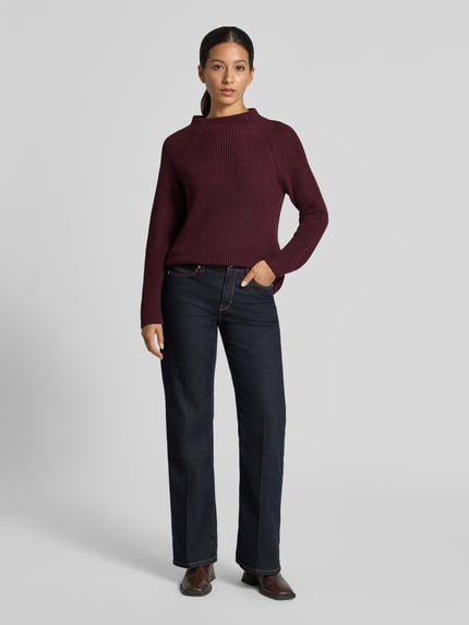 Frauenmodel trägt Strickpullover mit Stehkragen von monari in Dunkelrot, Grobstrick, kombiniert mit Jeans; Regular Fit, Baumwoll-Mix, Ganzkörperansicht von vorne.
