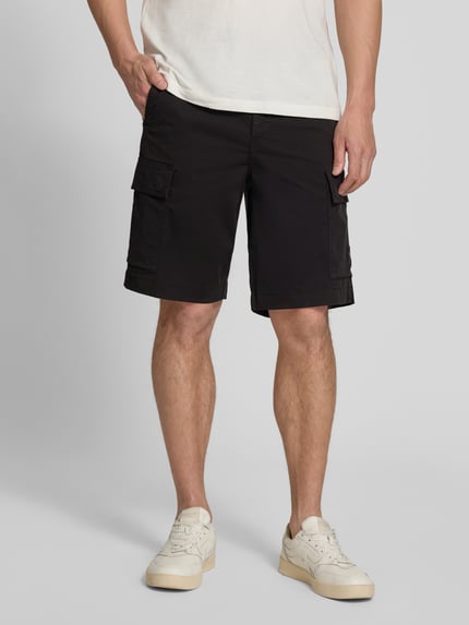 Männermodel trägt Relaxed Fit Cargoshorts aus katoenmix model 'SISLA' van BOSS Orange, effen zwart, cargozakken, knoop- en ritssluiting, label patch, voorkant, geheellichaamsaanzicht.