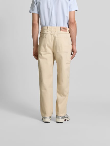 Mężczyznamodel nosi Straight Fit Jeans mit Cargo-Taschen von Kenzo, mieszanka bawełny, 5 kieszeni, kolor jasny beż, szerokość w rozmiarze 32: 76 cm, długość wewnętrzna nogawki: 45 cm, zapięcie na guzik i zamek błyskawiczny, widok całej sylwetki z tyłu.