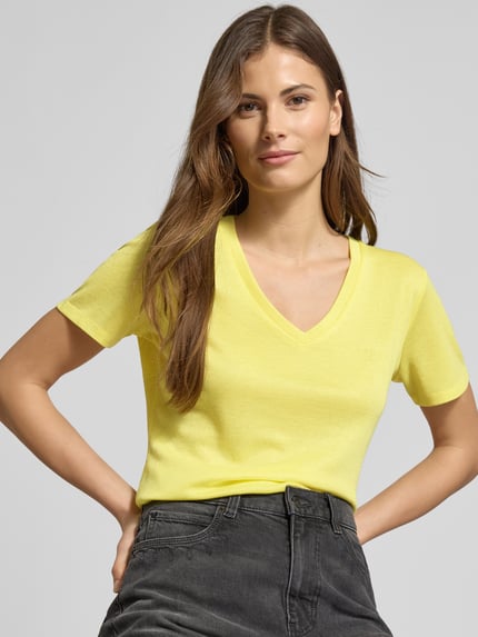Frauenmodel trägt Regular Fit T-Shirt aus Viskose-Mix von LIU JO SPORT in Gelb mit V-Ausschnitt, Glitzer-Optik, Logo-Detail, Nahaufnahme Oberkörper.