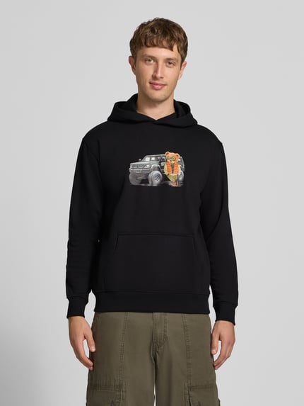 Männermodel trägt Relaxed Fit Hoodie aus Baumwoll-Mix mit Motiv-Print von CHILL PILL in Schwarz, Känguru-Tasche, Ganzkörperansicht von vorne.