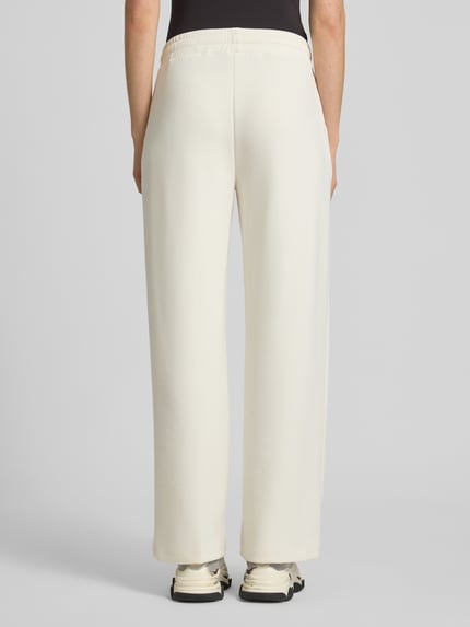 Frauenmodel trägt Sweatpants mit Label-Applikation Modell 'Talila' von JOOP! in Creme, gerader Schnitt, elastischer Bund, Ganzkörperansicht Rückansicht.