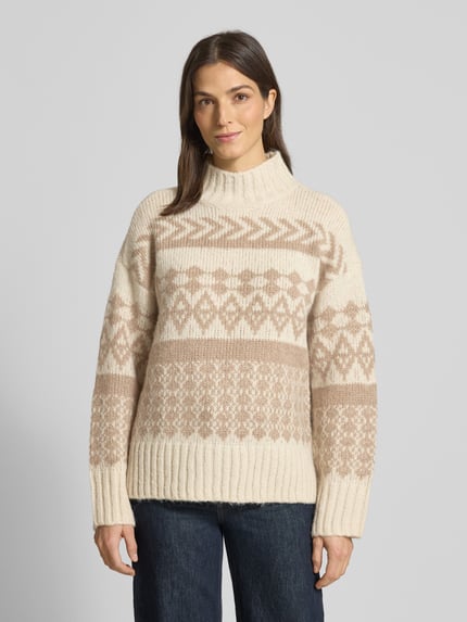 Frauenmodel trägt Comfort Fit Strickpullover aus Norweger-Strick Modell 'AMPLE' von Vero Moda, Optik:Allover-Muster, Stehkragen, Langarm, Ärmelabschluss gerippt, Rumpfabschluss gerippt, Materialverarbeitung: Strick, Farben Creme und Beige, Muster geometrisch, weiche Textur, Ganzkörperansicht von vorne.