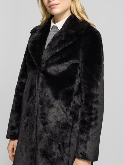 Frauenmodel trägt Relaxed Fit Mantel aus Kunstfell mit Eingrifftaschen von Christian Berg Woman Selection in Schwarz, Nahaufnahme Oberkörper. Mantelstruktur mit Reverskragen, glatte Textur, schlichte Linien, Kontext: Damen Mantel, Kunstfell, Relaxed Fit, Eingrifftaschen, Rückenlänge 95 cm, Schulterbreite 42 cm, Brustweite 50 cm, Ärmellänge 64 cm.