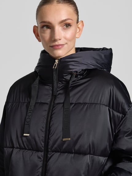 Frauenmodel trägt schwarzen Loose Fit Steppmantel mit Zweiwege-Reißverschluss von JOOP!, glatte Struktur, Nahaufnahme Oberkörper, Damen Steppmantel von JOOP!