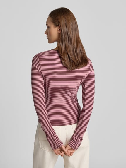 Frauenmodel trägt Longsleeve mit Henley-Kragen von REVIEW, eng anliegender Schnitt, Ripp-Struktur, Rückenlänge 50 cm, Ganzkörperansicht Rückansicht.