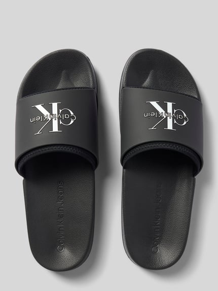 Produktfoto, czarne Badeschuhe mit Label-Prägung od CK Calvin Klein z białym logo, matowa faktura, widok z góry