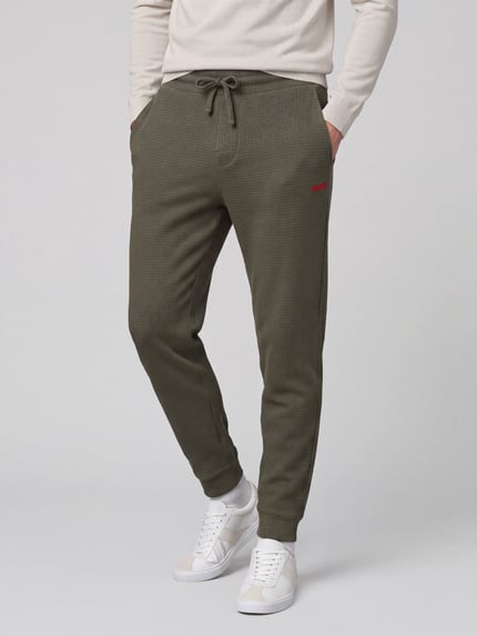 Mannenmodel draagt Regular Fit Sweathose aus Baumwoll-Mix Modell 'Austin' van HUGO, olijfgroen, ribstructuur, productfoto heren sweathose, detailopname onderlichaam, Ganzkörperansicht von vorne.