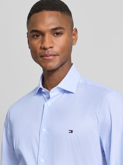 Männermodel trägt Slim Fit Businesshemd aus Baumwoll-Mix von Tommy Hilfiger, Optik:Allover-Muster, gestreift, Logo-Stitching, Nahaufnahme Oberkörper.