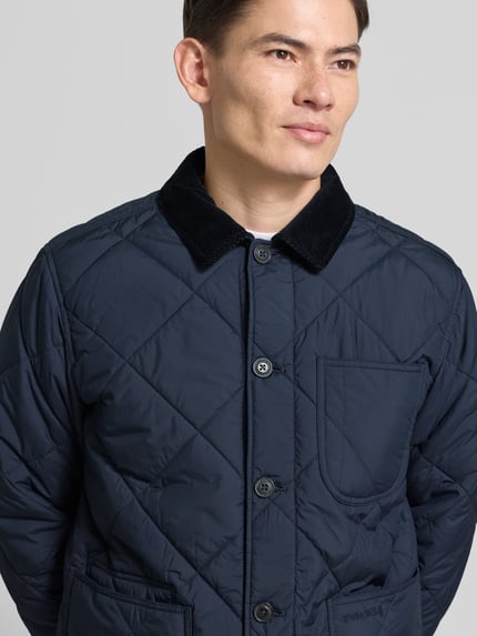 Männermodel trägt Regular Fit Steppjacke mit Kentkragen von Polo Ralph Lauren, Dunkelblau, Knopfleiste, Brusttasche, Label-Stitching, Nahaufnahme Oberkörper.