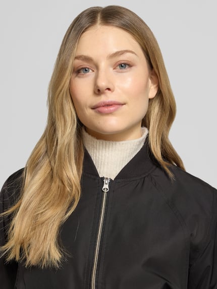 Vrouwenmodel draagt zwarte Regular Fit Jacke met opstaande kraag model 'Zaymi' van CARS JEANS, met steekzakken en ritssluiting, detailopname bovenlichaam.