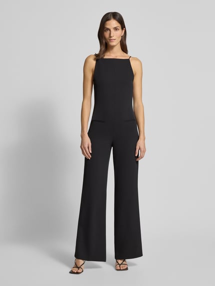 Frauenmodel trägt Jumpsuit mit Eingrifftaschen von Mango in Schwarz, lockerer Schnitt, Square-Neck, Ganzkörperansicht von vorne.
