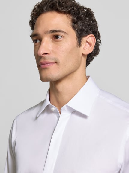 Männermodel trägt Regular Fit Businesshemd mit Satinstruktur von BOSS in Weiß, unifarben, Kentkragen, Nahaufnahme Oberkörper.
