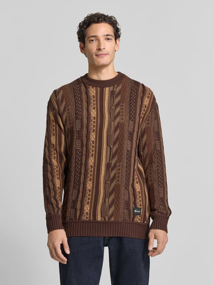 Männermodel trägt Regular Fit Strickpullover aus reiner Baumwolle von COLUCCI in Brauntönen mit Stehkragen, gerippten Abschlüssen, Ganzkörperansicht von vorne.