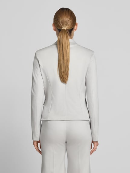 Frauenmodel trägt Slim Fit Blazer mit Pattentaschen von Marc Cain, Material-Mix mit Baumwoll-Anteil, Farbe hellgrau, Ganzkörperansicht Rückansicht. Rückenlänge bei Größe 36: 54 cm, Brustweite 35 cm, Ärmellänge 63 cm, Reverskragen, Knopfverschluss.
