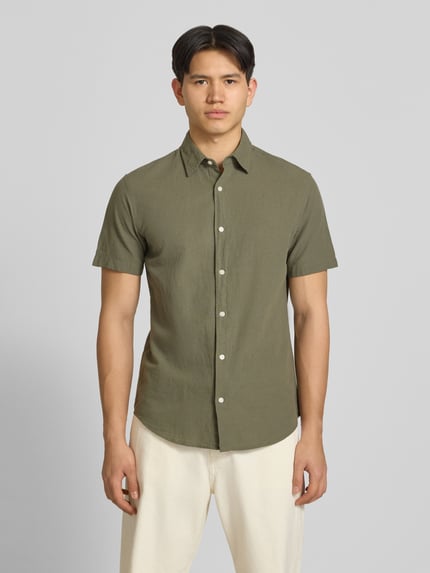 Männermodel trägt Regular Fit Freizeithemd aus Baumwoll-Leinen-Mix von Jack & Jones in Olivgrün, Knopfleiste, Kentkragen, Ganzkörperansicht von vorne.