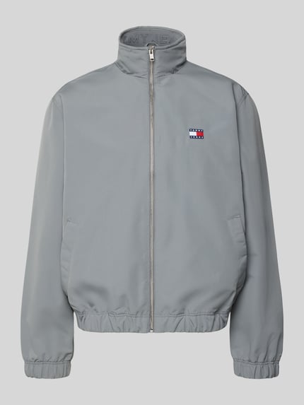 Produktfoto, Regular Fit Bomberjacke mit Label Stitching von Tommy Jeans in Optik: Unifarben, Stehkragen, Reißverschluss, Langarm, elastischer Ärmelabschluss, elastischer Rumpfabschluss, Innentasche, Eingrifftaschen mit Druckknopf, glatte Oberfläche, kühles Grau.