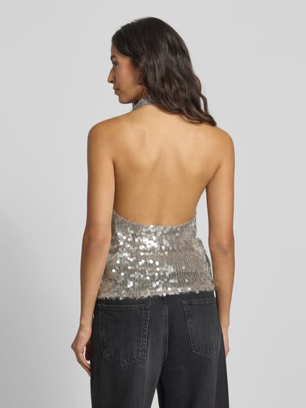Frauenmodel trägt Blusentop mit Neckholder von Mango in Silber mit Paillettenbesatz, Viskose-Mix mit Stretch-Anteil, lockerer Schnitt, Rückenlänge 24 cm, Ganzkörperansicht Rückansicht.