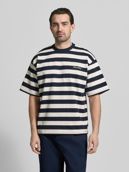 Männermodel trägt Relaxed Fit T-Shirt mit Logo-Stitching Modell 'Beam' von Woodbird aus reiner Baumwolle, Rundhalsausschnitt, Ganzkörperansicht von vorne.