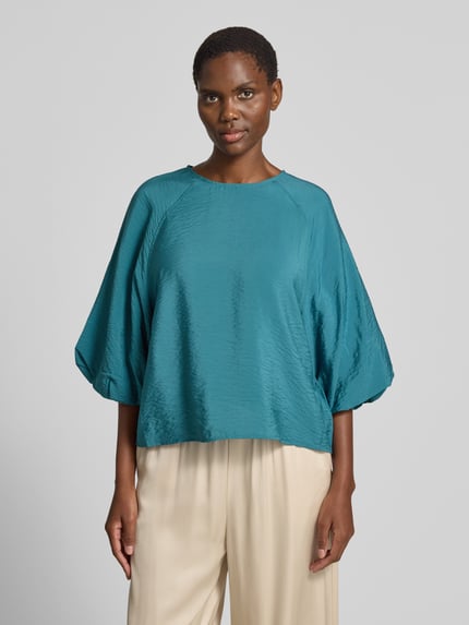 Frauenmodel trägt Regular Fit Bluse aus Viskose-Mix mit 3/4-Arm von Christian Berg Woman in Türkis mit Rundhalsausschnitt, Ganzkörperansicht von vorne. Rückenlänge bei Größe 36: 56 cm, Ärmellänge bei Größe 36: 44 cm, glatte Textur, weite Form.