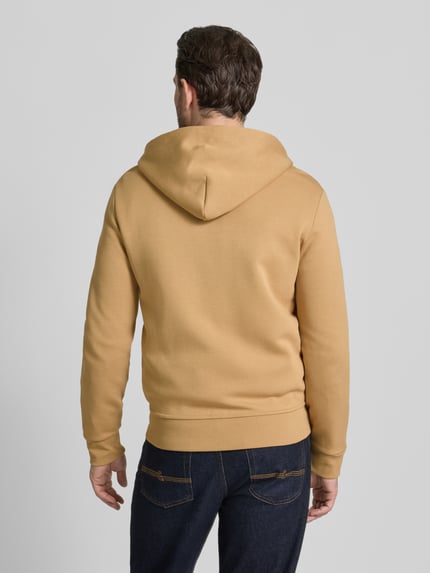 Männermodel trägt Sweatjacke mit Kapuze von Polo Ralph Lauren in Beige, Baumwoll-Elasthan-Mix, Regular-Fit, gerippte Abschlüsse, Rückenlänge 68 cm, Ärmellänge 65 cm, Eingrifftaschen, Label-Stitching, Reißverschluss, Ganzkörperansicht Rückansicht.