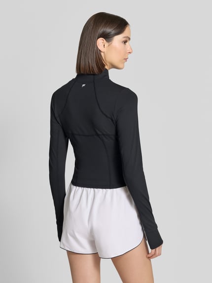 Frauenmodel trägt Slim Fit Jacke mit Stehkragen Modell 'STORM' von Fabletics, schwarze Farbe, glatte Textur, Ganzkörperansicht Rückansicht, Rückenlänge 45 cm, Schulterbreite 35 cm, Brustweite 42 cm, Ärmellänge 68 cm.