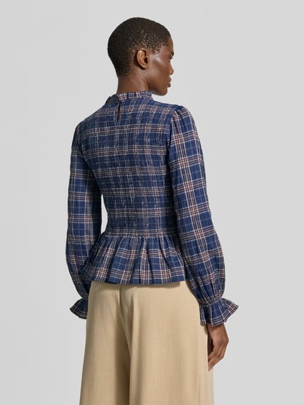 Frauenmodel trägt Bluse mit Smok-Details und Rüschenärmeln von Christian Berg Woman Selection, kariertes Muster in Blau und Beige, Baumwoll-Mix mit Stretch-Anteil, taillierter Schnitt, Rückenlänge 58 cm, Ärmellänge 64 cm, Ganzkörperansicht Rückansicht.