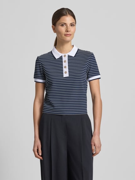 Vrouwenmodel draagt Cropped Poloshirt uit viscosemix model 'ALPHONSINE' van Guess, kort, streepmotief, knoopsluiting, ruglengte maat S 49 cm, voorkant volledige lichaamsopname.