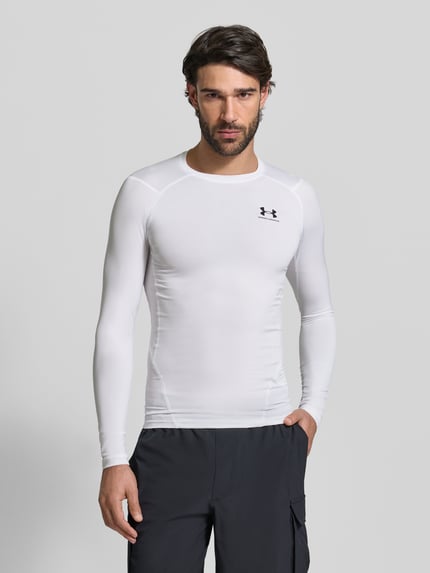 Männermodel trägt weißes Slim Fit Longsleeve mit Logo-Print von Under Armour aus elastischem Material, Rundhalsausschnitt, Ganzkörperansicht von vorne