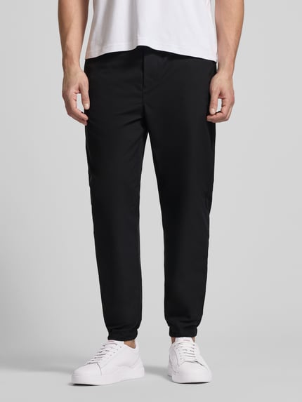 Männermodel trägt Slim Fit Schlupfhose mit Gesäßtasche von CK Calvin Klein in Schwarz, elastischer Bund, glatte Textur, Nahaufnahme Oberkörper.