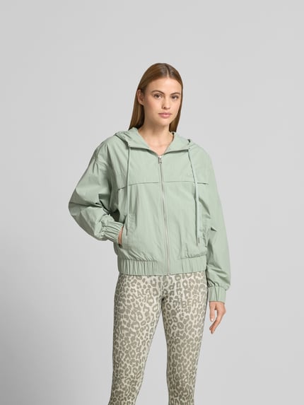 Vrouwenmodel draagt Regular Fit Jacke mit Logo-Stitching van Lala Berlin in lichtgroen met capuchon, tunnelkoord, steekzakken, ritssluiting, ruglengte bij maat S 53 cm, borstwijdte 60 cm, mouwlengte 59 cm, Ganzkörperansicht van voren.