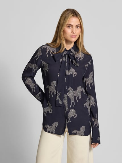 Frauenmodel trägt Relaxed Fit Bluse aus reiner Viskose Modell 'ODETTA' von ODETTA mit Allover-Motiv-Print, dunkelblau-creme, Zierschleife, Langarm, Ganzkörperansicht von vorne.