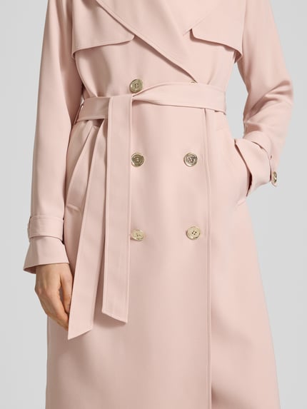Vrouwenmodel draagt Zweireihiger Trenchcoat mit Bindegürtel van MICHAEL Michael Kors in lichtroze, regular fit, reverskraag, dubbele knopenrij, ceintuur, gladde textuur, detailopname van het bovenlichaam.