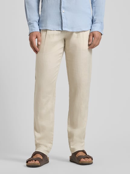 Mannenmodel draagt Tapered Leinenhose mit Gürtelschlaufen Modell 'OSBY JOGGER' van Marc O'Polo, effen lichtbeige linnen met bandplooi, riemlussen, knoopsluiting, zijzakken en achterzakken, pure linnen textuur, volledige lichaamsopname van voren.