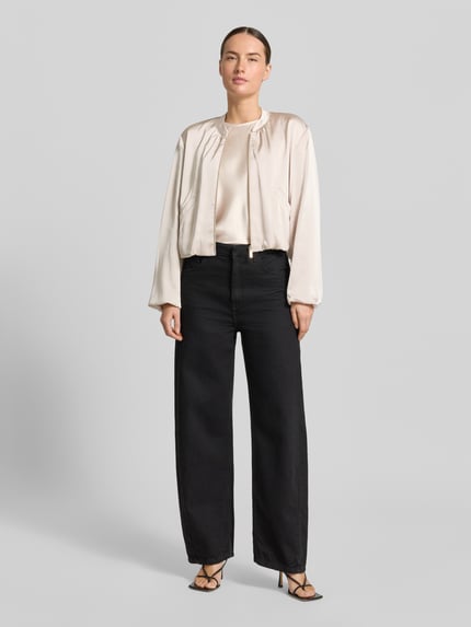 Modelka nosi Regular Fit Blazer aus Satin mit Reißverschluss von Betty Barclay, satyna, krój regular fit, stójka, zamek błyskawiczny, wpuszczane kieszenie, długość tyłu w rozmiarze 36: 50 cm, szerokość w rozmiarze 36: 56 cm, długość rękawów w rozmiarze 36: 58 cm, jasny beż, czarne spodnie, subtelna satynowa powierzchnia, cała sylwetka z przodu